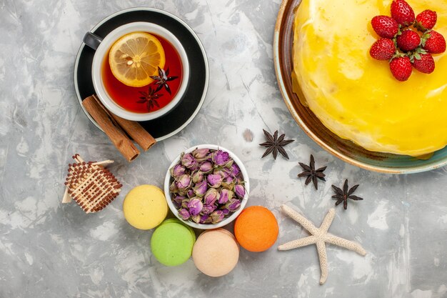 Vista superior delicioso pastel afrutado con jarabe amarillo macarons franceses y una taza de té en la superficie blanca galleta de pastel dulce azúcar hornear galleta de té