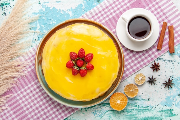 Vista superior delicioso pastel con almíbar amarillo fresas rojas frescas y una taza de té en la superficie azul pastel de galletas hornear galletas dulces té de azúcar