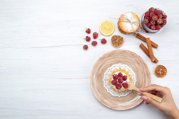 Vista superior del delicioso pastel con crema y frambuesas junto con galletas de sándwich de canela en el piso de luz pastel de frutas y bayas galleta dulce