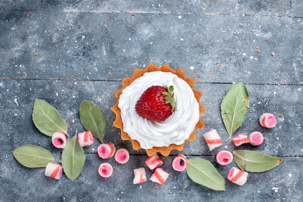 Vista superior del delicioso pastel cremoso con fresas frescas y caramelos rosados en rodajas sobre gris, pastel dulce crema para hornear dulces de frutas