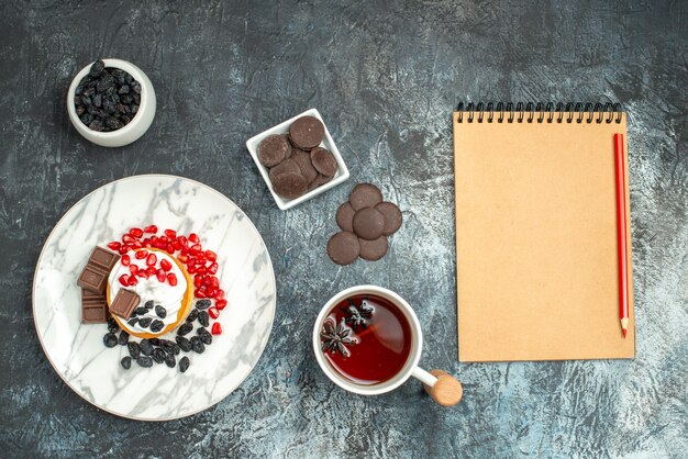 Vista superior delicioso pastel cremoso con galletas choco y taza de té en el fondo claro-oscuro