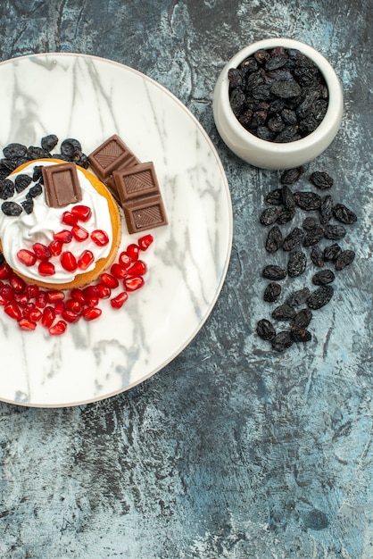 Vista superior delicioso pastel cremoso con granadas de chocolate y pasas sobre fondo claro-oscuro