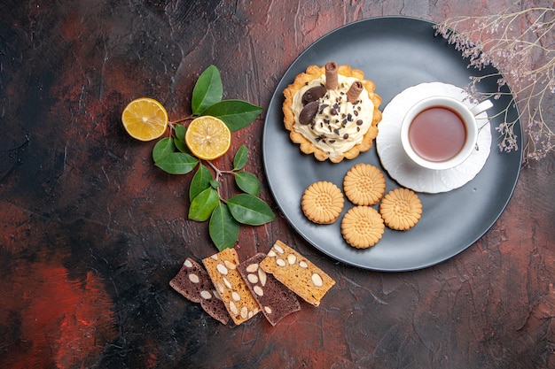 Vista superior delicioso pastel cremoso con taza de té en el postre dulce pastel de mesa oscura