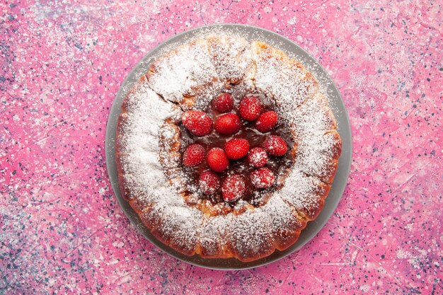 Vista superior del delicioso pastel de fresa con azúcar en polvo en la superficie de color rosa claro