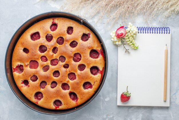 Vista superior del delicioso pastel de fresa horneado con fresas rojas frescas en el interior con pan y bloc de notas en el escritorio blanco, pastel, galleta, fruta, hornear dulce