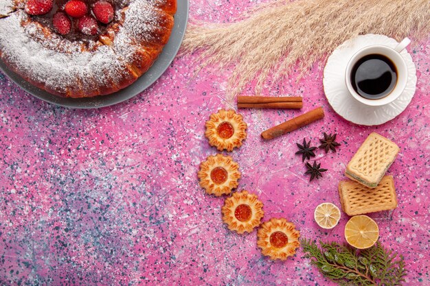 Vista superior delicioso pastel de fresa pastel de azúcar en polvo con waffles pequeñas galletas y taza de té en pastel de escritorio rosa pastel de galletas de azúcar dulce