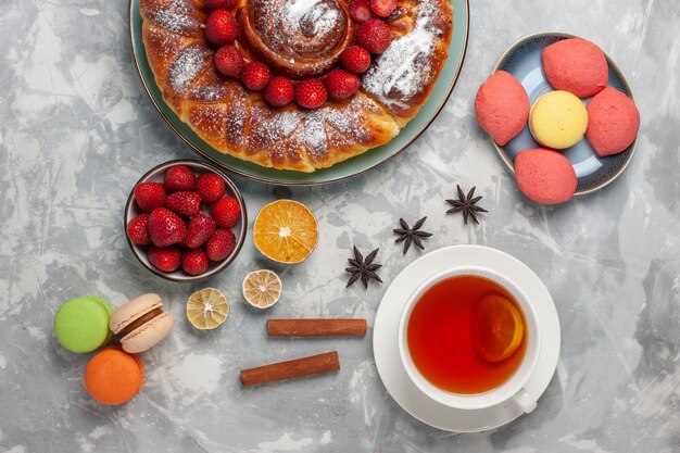 Vista superior delicioso pastel de fresa con pasteles pequeños y una taza de té en la superficie blanca pastel de azúcar de galleta pastel de hornear dulce