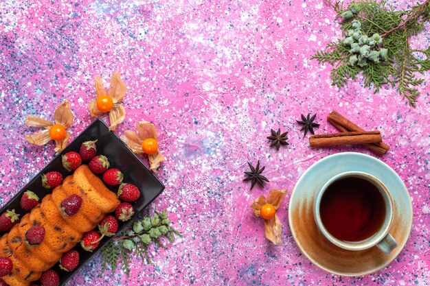 Vista superior delicioso pastel con fresas rojas y taza de té en el escritorio rosa.