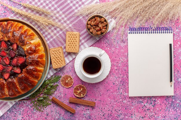 Vista superior del delicioso pastel de fresas con sabor a fruta con una taza de té en la rosa