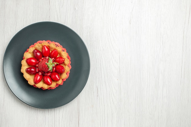 Vista superior del delicioso pastel con frutas frescas dentro de la placa en el escritorio blanco