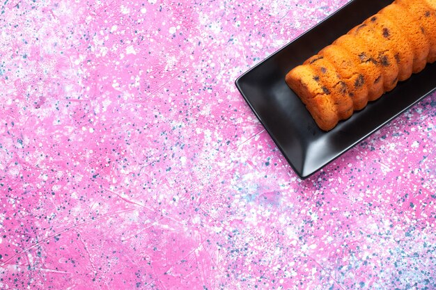 Vista superior delicioso pastel horneado dentro de un molde para pastel negro sobre el escritorio rosa.