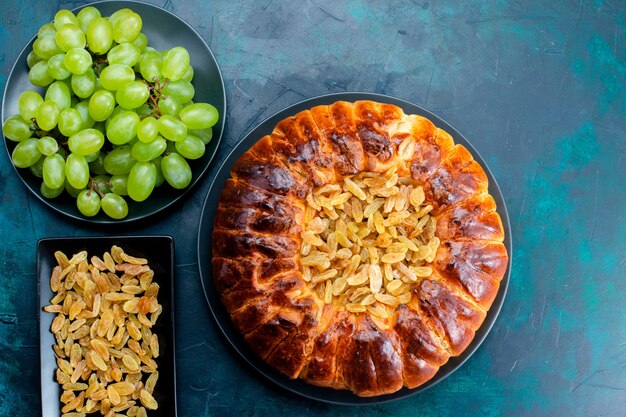 Vista superior delicioso pastel horneado con pasas y uvas verdes frescas sobre el fondo azul oscuro pastel de azúcar dulce masa de galleta