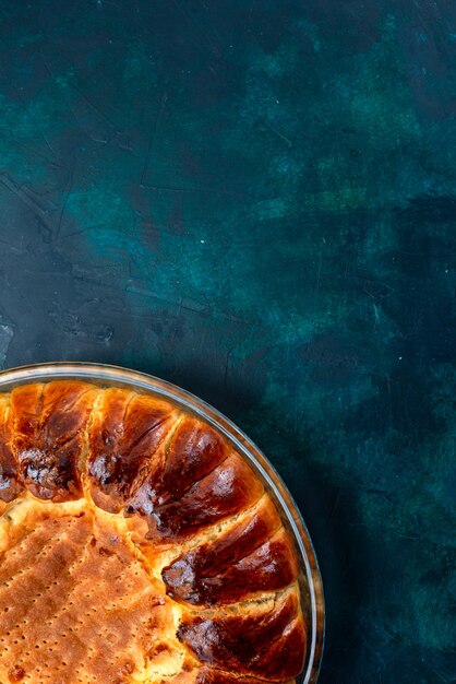 Vista superior delicioso pastel horneado redondo formado dulce dentro de la bandeja de vidrio sobre el fondo azul claro.