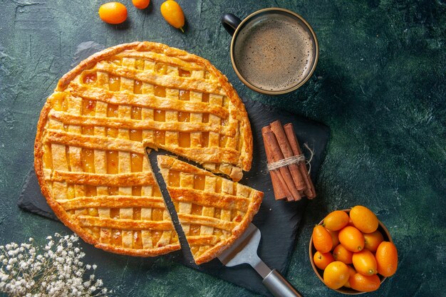 Vista superior delicioso pastel de kumquat con una pieza en rodajas y café sobre fondo oscuro