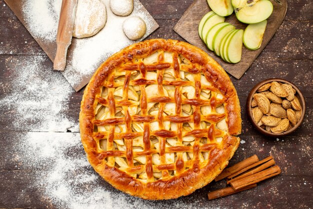 Una vista superior del delicioso pastel de manzana de forma redonda con canela, manzanas frescas y masa sobre el fondo oscuro, pastel, galleta, azúcar, fruta