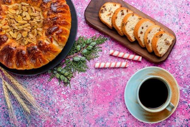 Vista superior del delicioso pastel de pasas con una taza de café sobre fondo rosa hornear pastel de azúcar galletas dulces galletas color