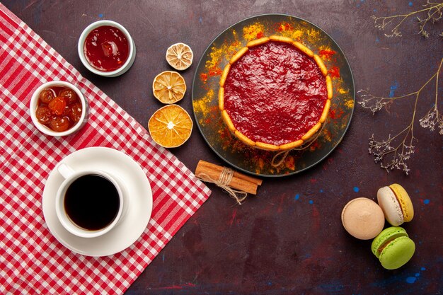 Vista superior del delicioso pastel de postre con taza de macarons de café y mermeladas de frutas en el escritorio oscuro galletas de azúcar pastel postre dulce