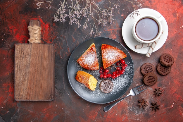 Vista superior del delicioso pastel en rodajas con una taza de té en el té de pastel dulce de pastel de mesa oscura