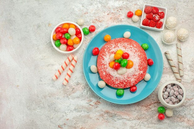 Vista superior del delicioso pastel rosa con caramelos de colores en el escritorio blanco, postre, pastel de golosinas de arco iris de colores