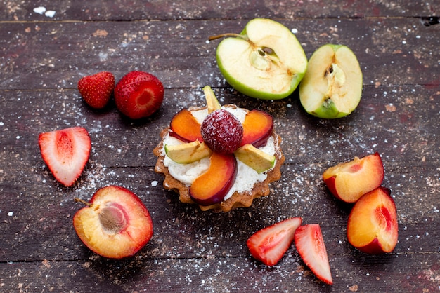 Una vista superior del delicioso pastelito con crema y frutas frescas en rodajas en el escritorio marrón, pastel de frutas, té de galletas