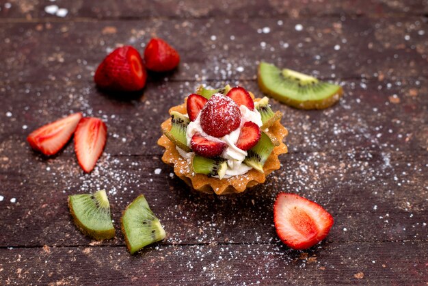 Una vista superior delicioso pastelito con crema y frutas frescas en rodajas en la galleta de pastel de frutas de fondo marrón