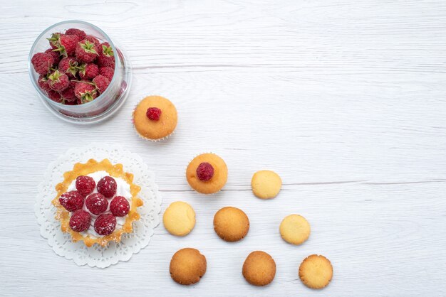 Vista superior del delicioso pastelito con frambuesas junto con fresas y galletas a la luz, baya dulce de galleta de pastel