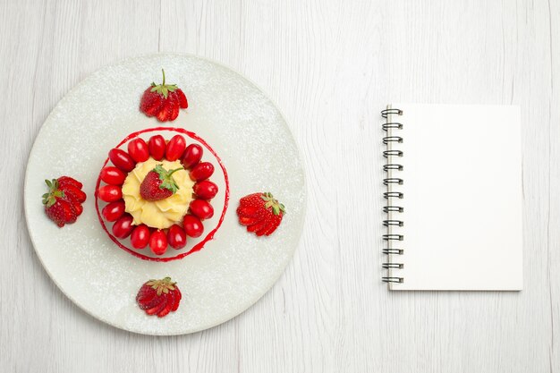 Vista superior del delicioso pastelito con frutas dentro de la placa en el escritorio blanco