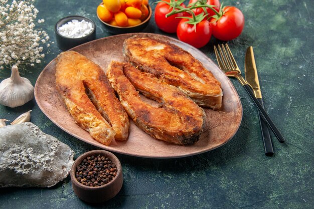 Vista superior del delicioso pescado frito en un plato marrón y cubiertos, especias, alimentos en una mesa de colores mezclados con espacio libre