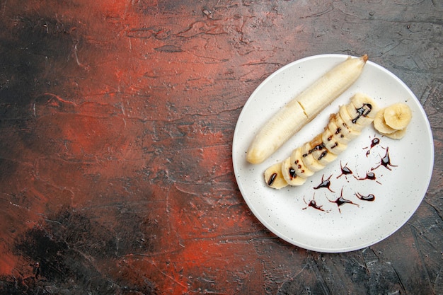 Vista superior delicioso plátano con trozos en rodajas dentro de la placa sobre el fondo oscuro