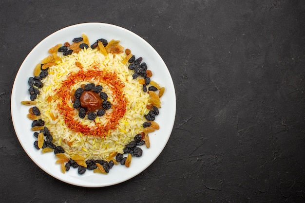 Vista superior delicioso plov con aceite y pasas dentro de la placa en el espacio oscuro