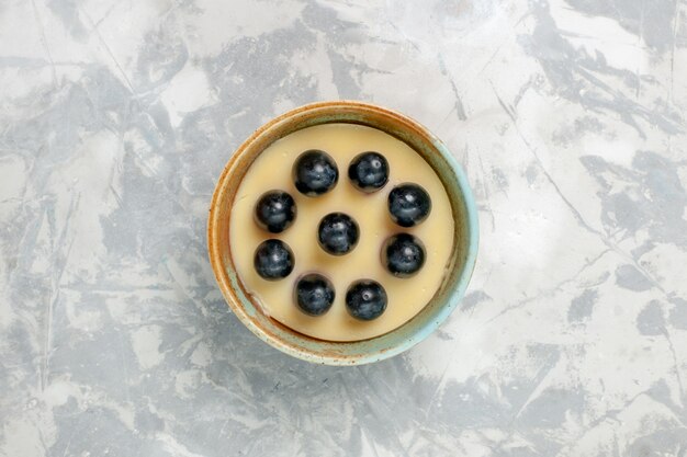 Vista superior del delicioso postre de crema con uvas en la parte superior dentro de una pequeña olla en la superficie blanca postre helado crema dulce