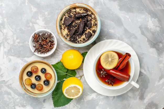 Vista superior delicioso postre cremoso de galleta con taza de té y limón sobre superficie blanca galletas de frutas pastel dulce de azúcar de galleta