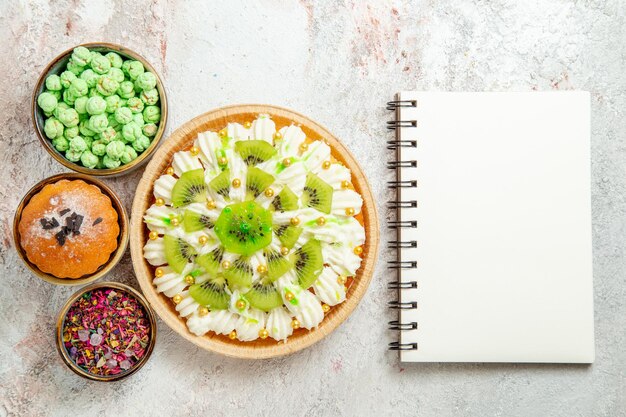 Vista superior delicioso postre con kiwis en rodajas y caramelos sobre fondo blanco pastel de galletas postre crema de frutas dulces