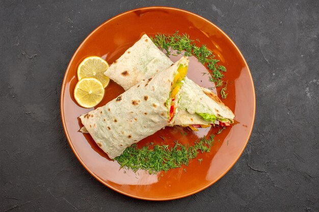 Vista superior delicioso sándwich de ensalada shaurma en rodajas con rodajas de limón dentro de la placa sobre un fondo oscuro comida de hamburguesa bocadillo pan de sándwich