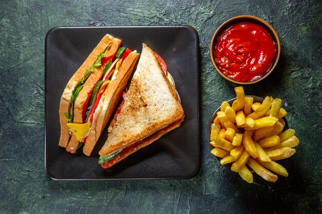 Vista superior delicioso sándwich de jamón dentro de un plato oscuro con papas fritas y salsa de tomate en una superficie oscura