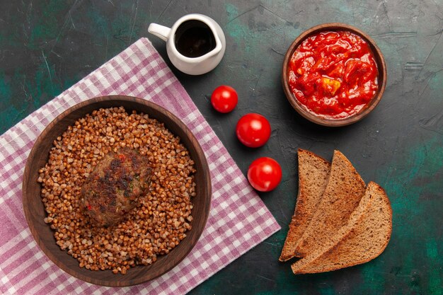 Vista superior delicioso trigo sarraceno cocido con chuletas y hogazas de pan en el plato de verduras de comida de ingrediente de superficie verde oscuro