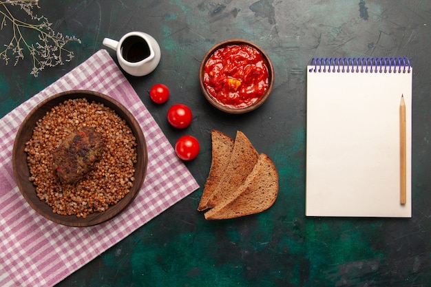 Vista superior delicioso trigo sarraceno cocido con hogazas de pan y chuleta en el plato de verduras de comida de ingrediente de superficie verde oscuro