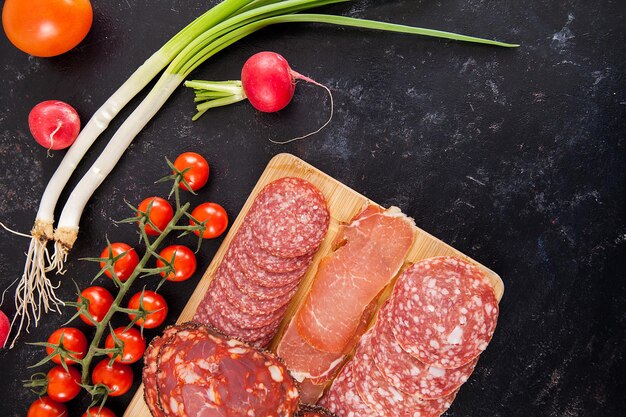 Vista superior de deliciosos aperitivos de carne saludables en tablero de madera junto a tomates cherry, rábano y cebolla verde
