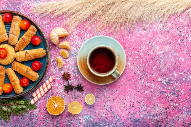 Vista superior de deliciosos bagels dulces dentro de la bandeja con ciruelas ácidas y té en el escritorio rosa claro