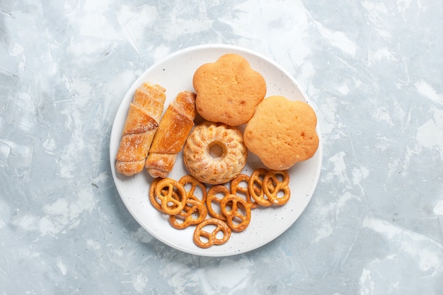 Vista superior deliciosos bagels con galletas y pasteles dentro de la placa en el escritorio blanco claro.