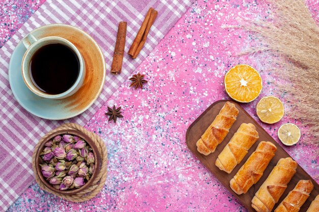 Vista superior deliciosos bagels con rodajas de limón y una taza de té en el escritorio de color rosa claro.