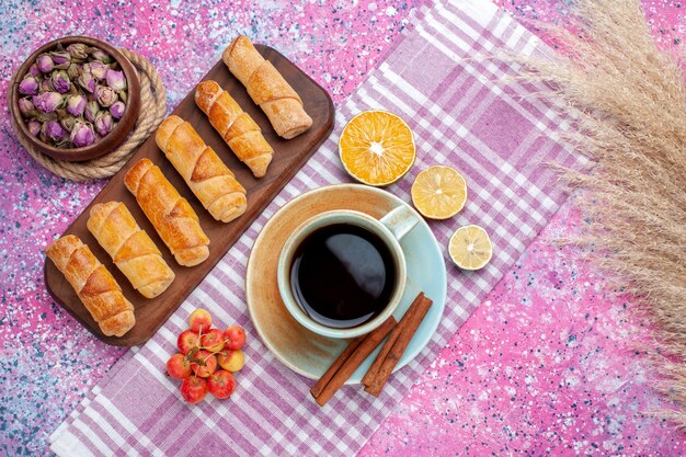 Vista superior deliciosos bagels con taza de té y limón en el escritorio de color rosa claro.