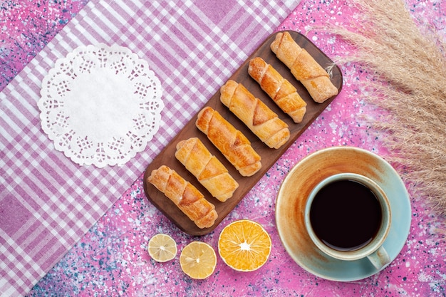 Vista superior deliciosos bagels con taza de té y limón en el escritorio de color rosa claro.