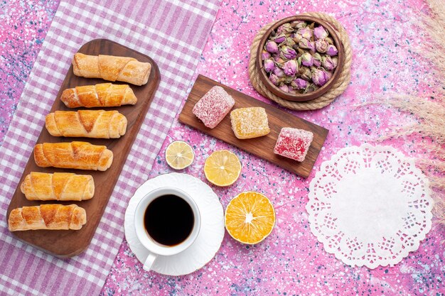 Vista superior deliciosos bagels con taza de té y mermeladas sobre fondo rosa claro.