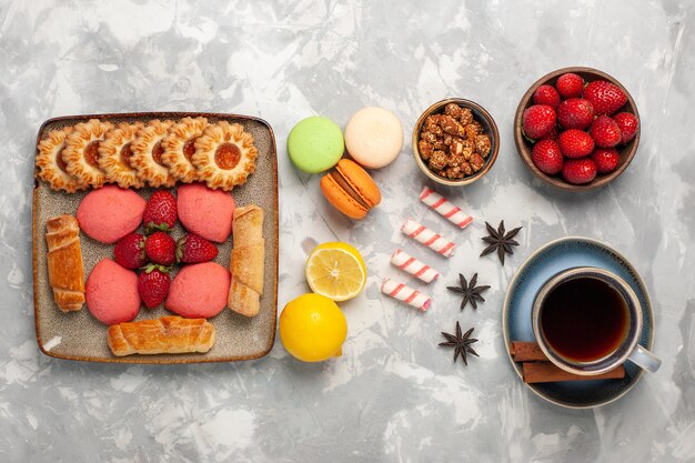 Vista superior deliciosos bagels con tortas, té, fresas frescas, té y galletas en el escritorio blanco