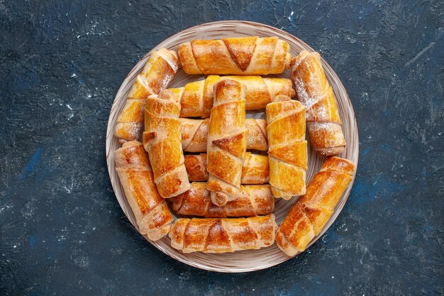 Vista superior deliciosos brazaletes dulces con relleno dentro de la placa en el escritorio oscuro pastel de galletas dulces hornear pasteles