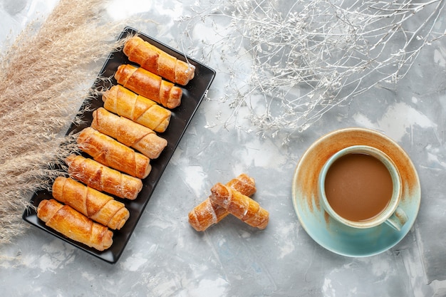 Vista superior de deliciosos brazaletes horneados dentro de molde negro con café con leche en gris, pastelería hornear galletas dulces