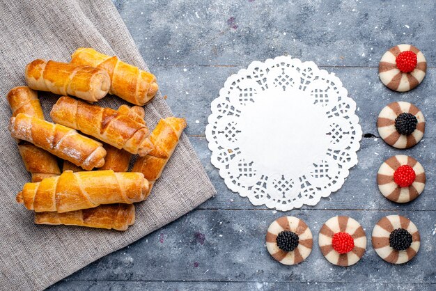 Vista superior deliciosos brazaletes con relleno junto con galletas en el fondo gris pastel hornear galleta dulce