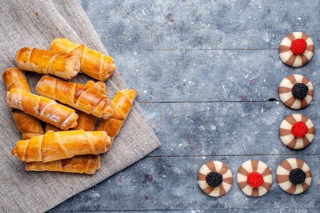 Vista superior deliciosos brazaletes con relleno junto con galletas en el fondo gris pastel hornear galletas azúcar dulce