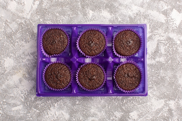 Foto gratuita vista superior de deliciosos brownies de chocolate dentro de un paquete morado sobre el fondo claro de chocolate dulce para hornear masa